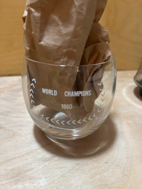 RARE 1960 Pittsburgh Pirates World Champions commemorative drinking glass with “WORLD CHAMPIONS 1960” and mascot illustration, stuffed with crumpled brown paper.