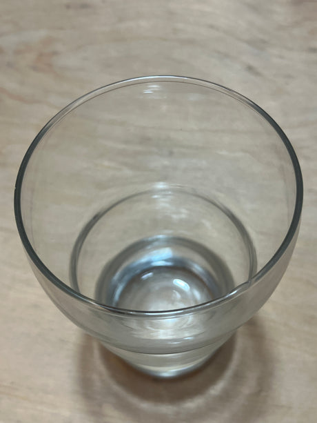 Wavy sided tall drinking glass partially filled with water on a light wood surface, showcasing its unique textured design and elegant shape.