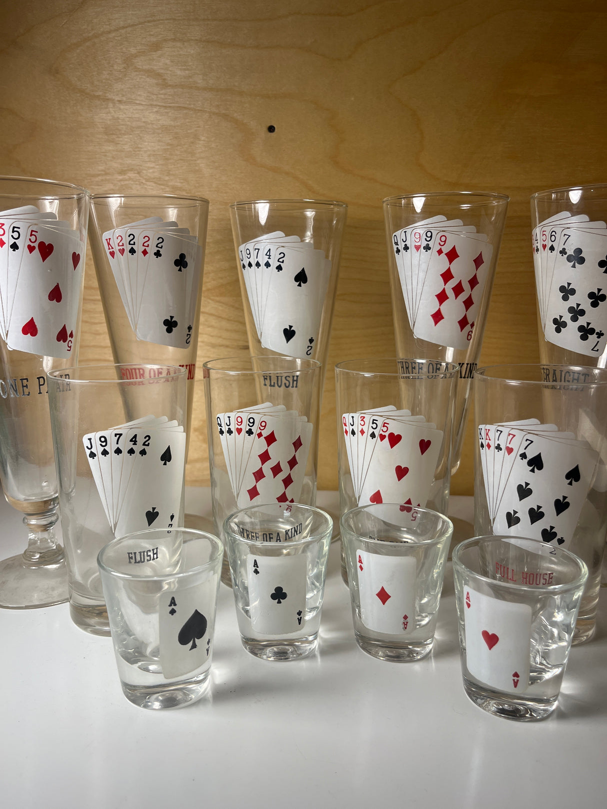 RARE 1960’s MCM poker-themed drinkware set featuring tall and shot glasses, each displaying unique five-card poker hands like Full House and Straight.