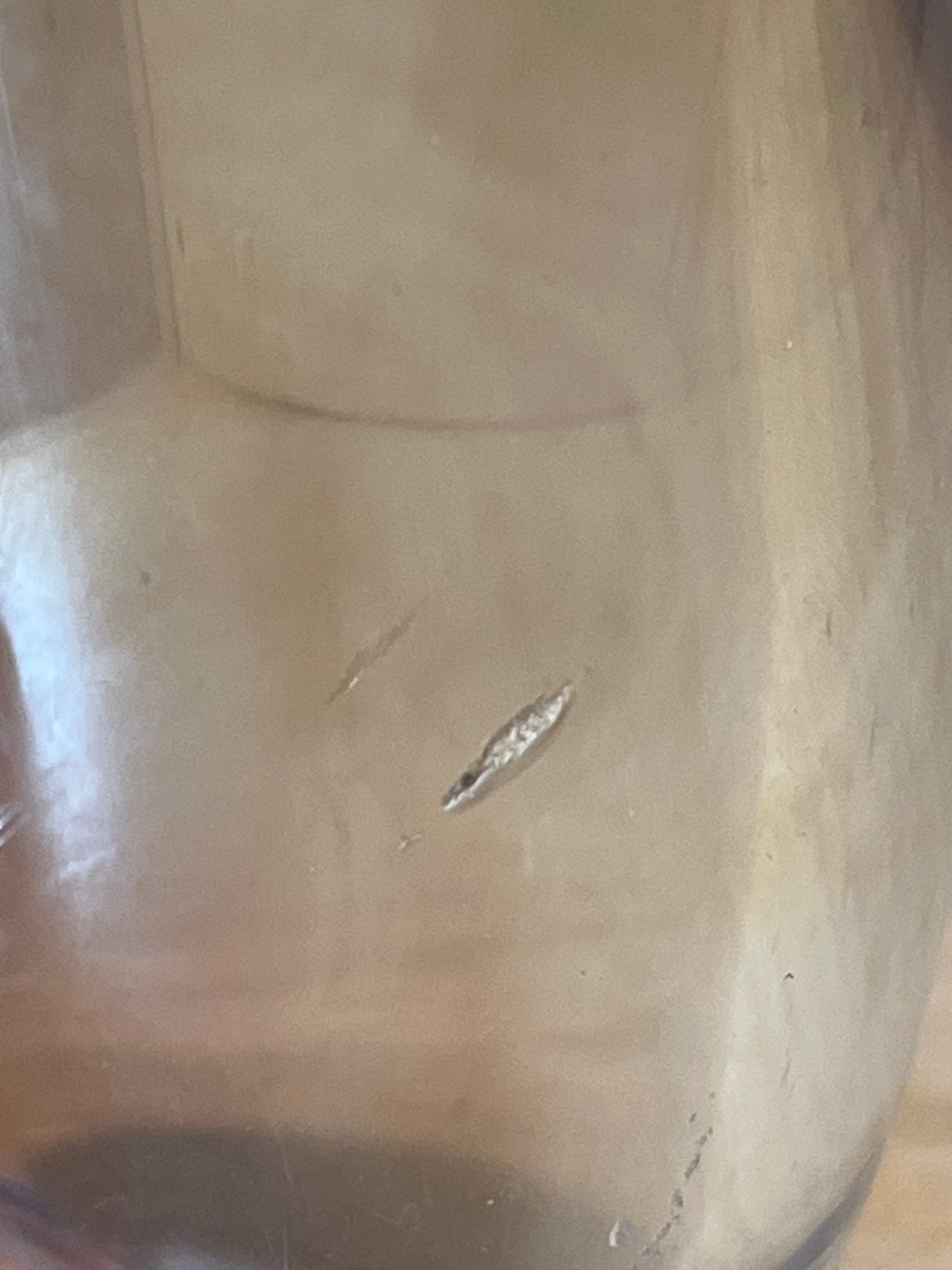 Close-up of a stemless hard acrylic wine glass interior showing two elongated gouges, revealing a lighter material beneath the scratched surface.