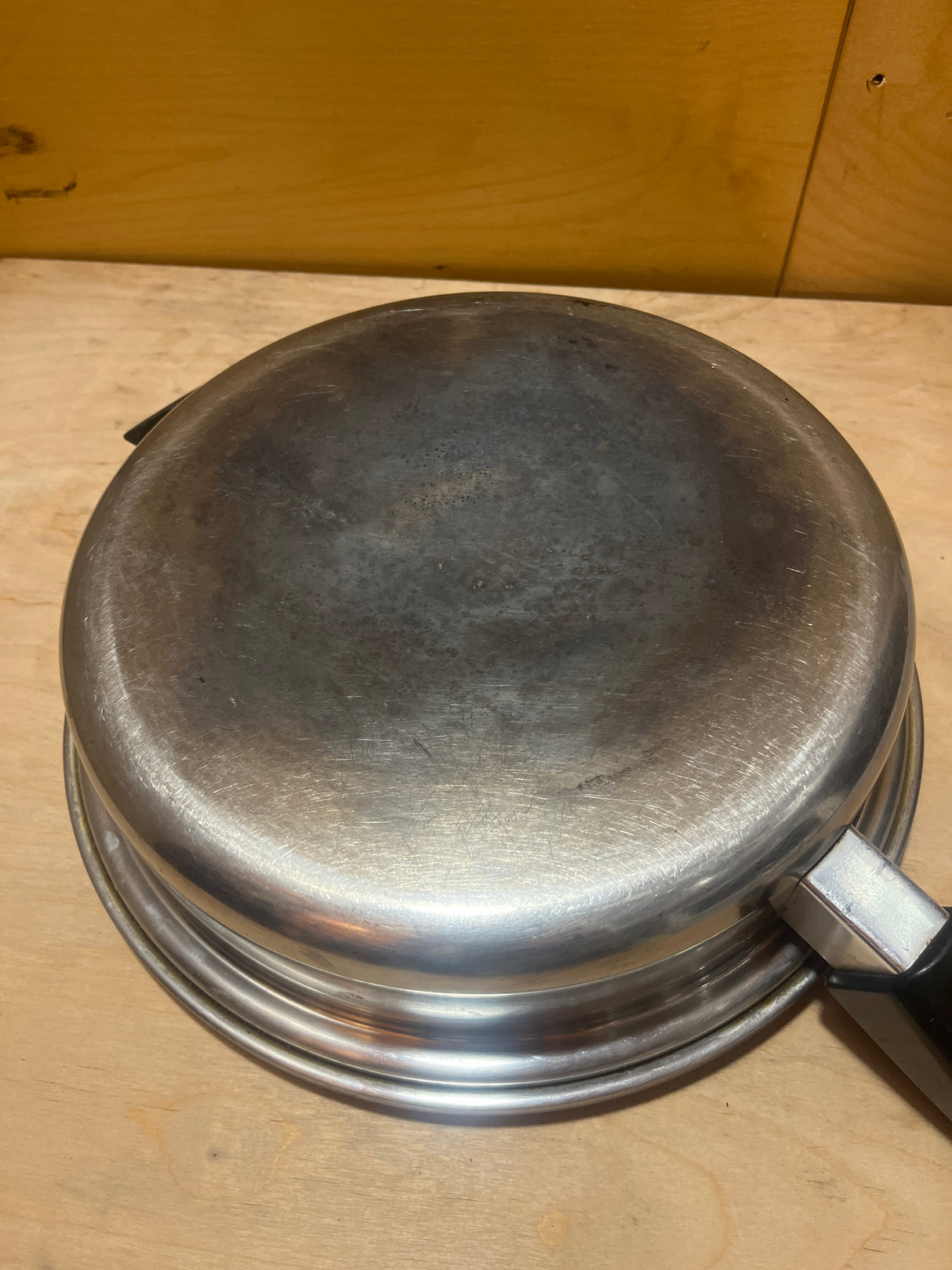 Seal-O-Matic Thermium Multi-Plex 18-8 Stainless Steel 11” Skillet, shown upside-down, highlighting its rounded bottom and side handle on a wooden surface.