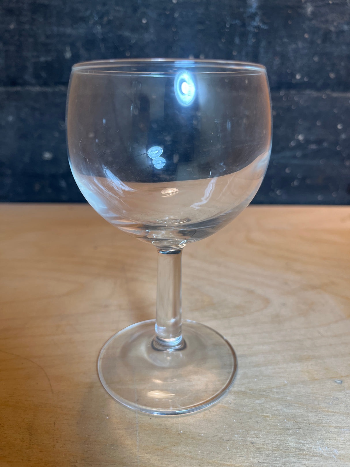 Libbey Embassy 6.5oz wine glass with a round bowl, straight stem, and flat foot, designed to be dainty and chip-resistant, on a wood surface.