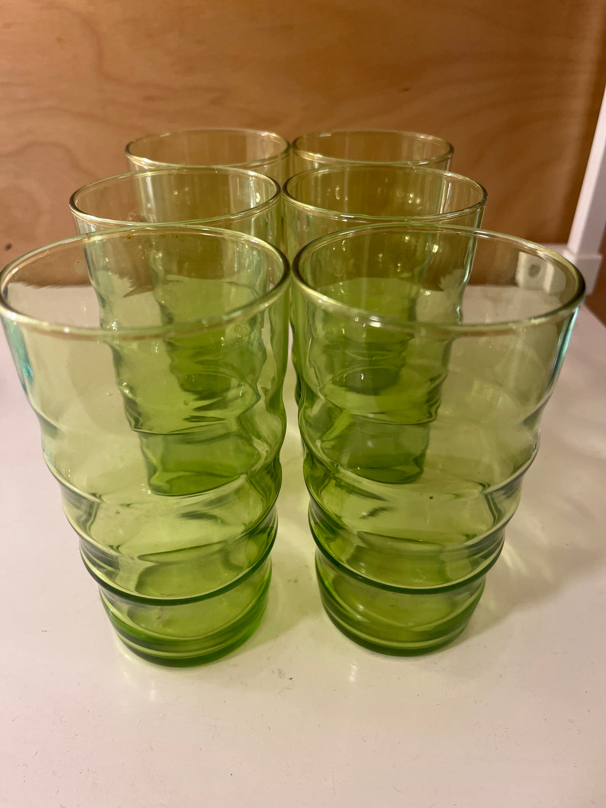 Set of 6 1970s wavy green glass tumblers with gently rippled texture, arranged neatly on a light surface, showcasing their tall, translucent design.