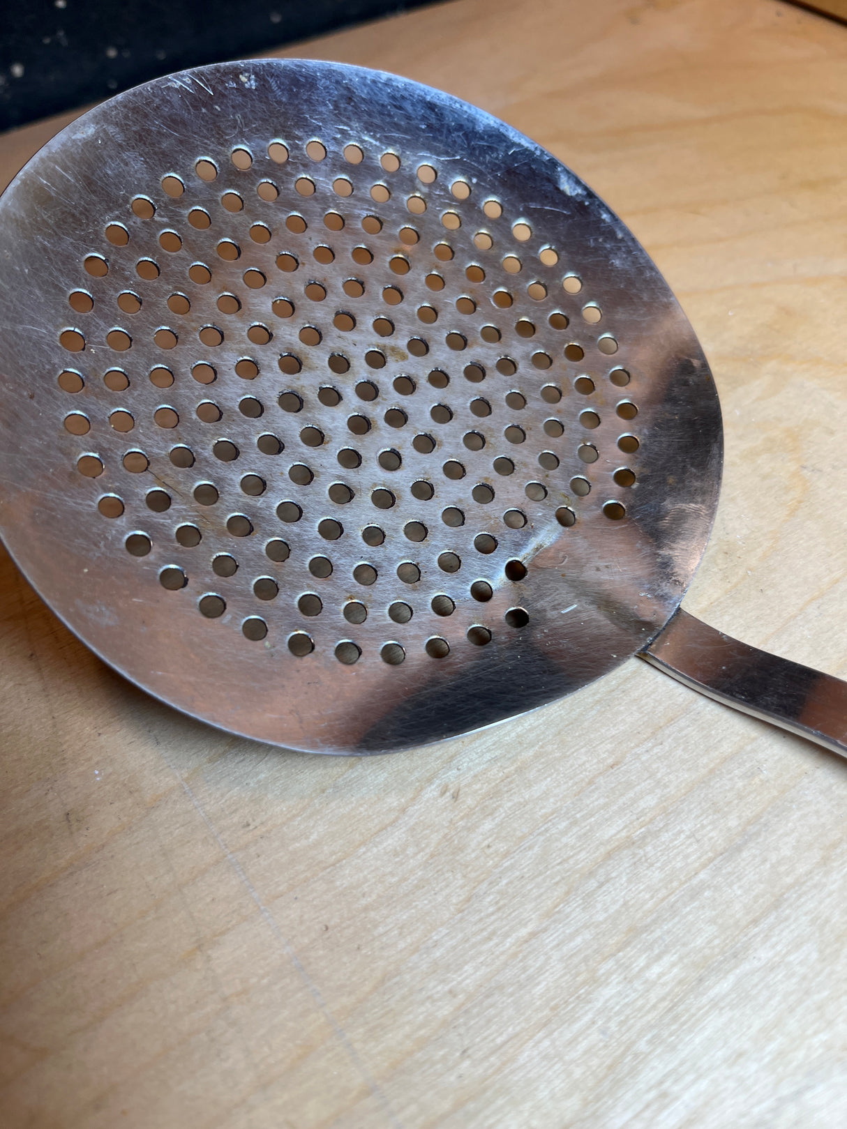 Round skimmer spoon - stainless steel with a white plastic handle, featuring minor heat damage on the handle tip, designed for safely lifting food from hot liquids.