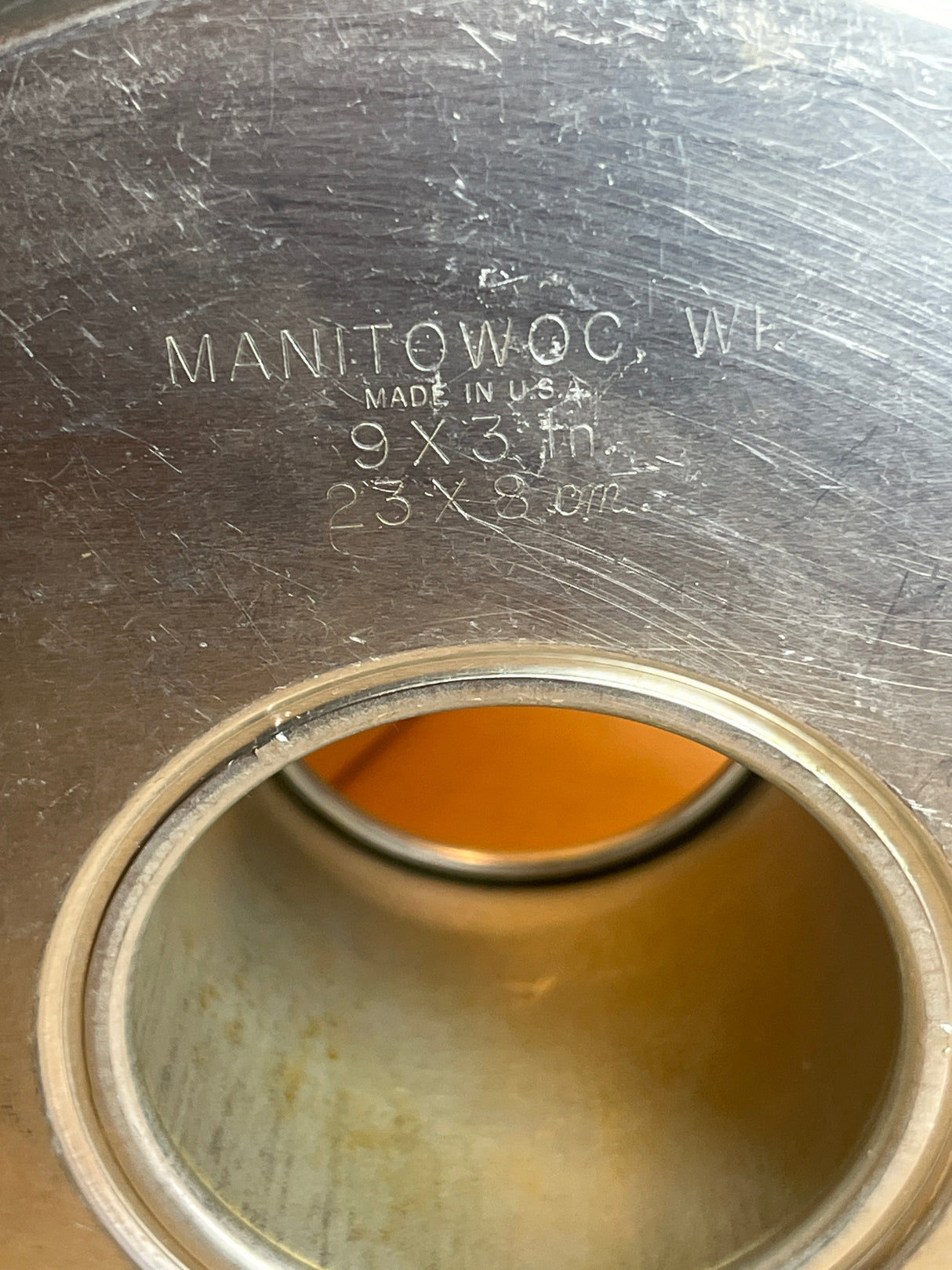 Close-up of a Manitowoc stainless-steel panel with factory stamp, featuring a circular cutout. Describes a Springform 3-piece angel food cake pan - vintage Manitowoc aluminum.