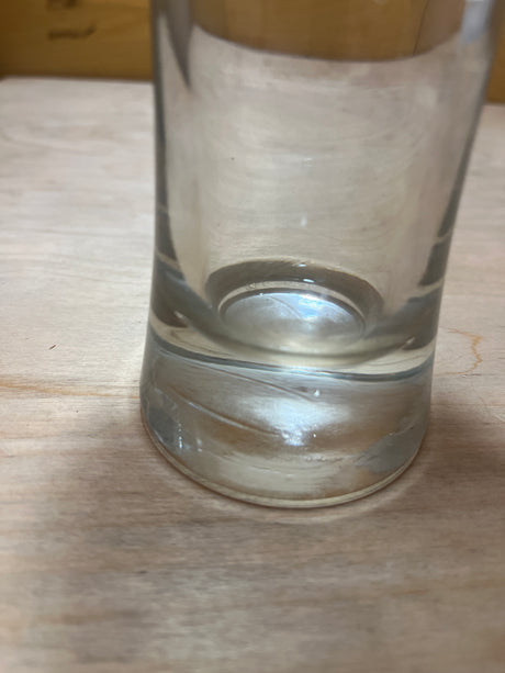 Tall Pilsner beer glass with a flared rim and sturdy weighted base, nearly empty, positioned on a wooden table.