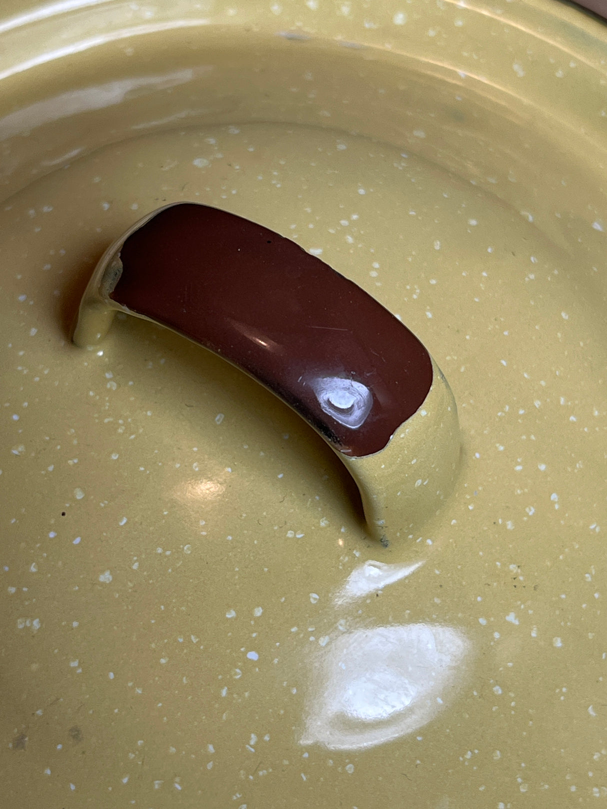Close-up of a Mini pot with lid and wire handle - vintage enamelware in yellow with brown accents, highlighting its speckled lid and curved brown handle.