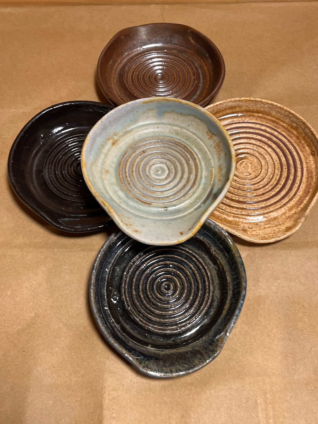 Handmade ceramic garlic grater spoon rests by Charles Lehman, featuring five hand-thrown dishes with pinched lips and circular ridges, showcasing varied glaze finishes.