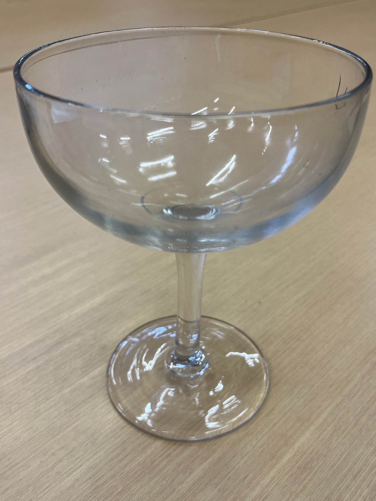 Large margarita/coupe glass on a table, containing liquid, highlighting its sleek design and transparent material, perfect for elegant drink presentation.