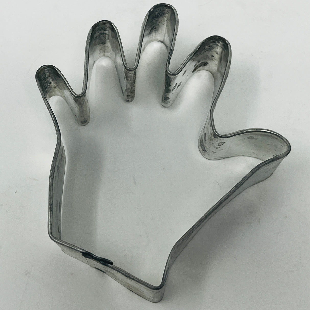 Mid-century metal cookie cutter in a hand shape, featuring an adaptive design with a large handle for easy gripping, suitable for various themed cookie creations.
