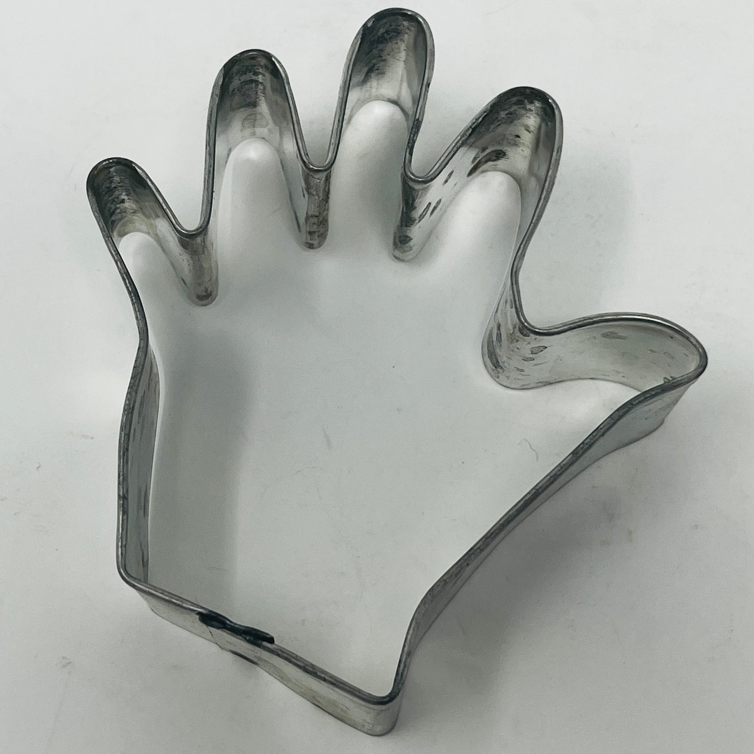 Mid-century metal cookie cutter in a hand shape, featuring an adaptive design with a large handle for easy gripping, suitable for various themed cookie creations.