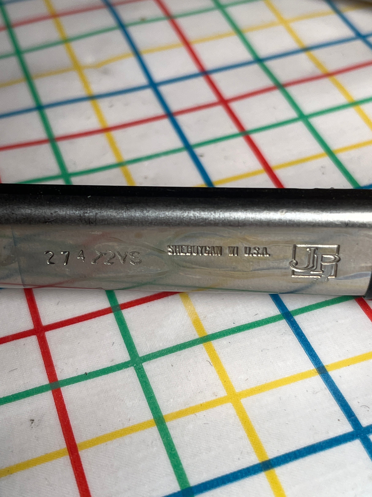 Close-up of metal piece from Large 16” restaurant serving tongs, Vollrath 4791620, with “274 X2VS,” “SHEBOYGAN WI USA,” and JP logo, on a grid mat.