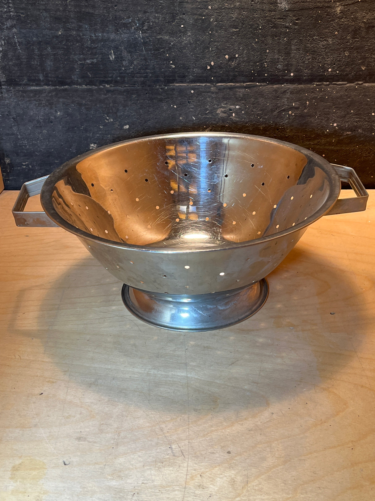 Vintage stainless steel colander with flat handles, a raised base, and small drain holes, ideal for single servings. Reflective surface adds charm.