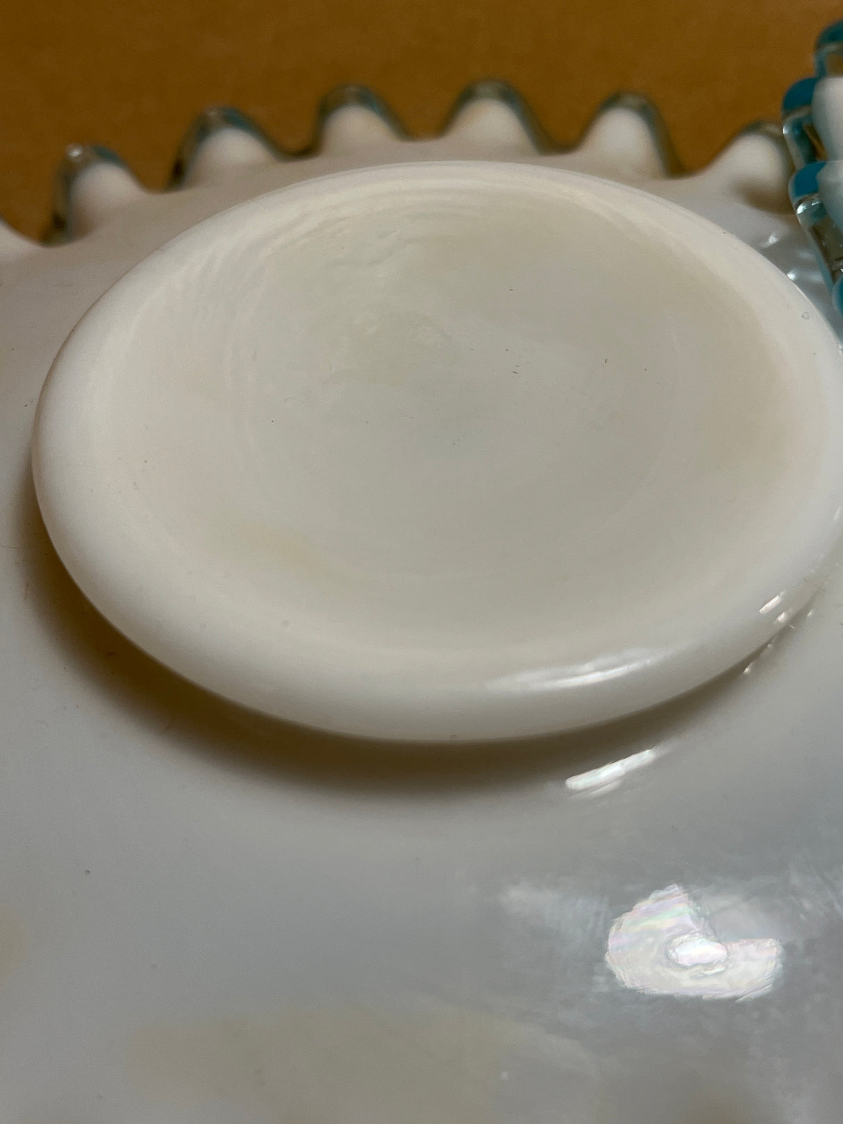 Bowl n plate set featuring a glossy white ceramic lid or saucer atop a larger scallop-edged dish, with a hint of a blue-and-white beaded object visible.