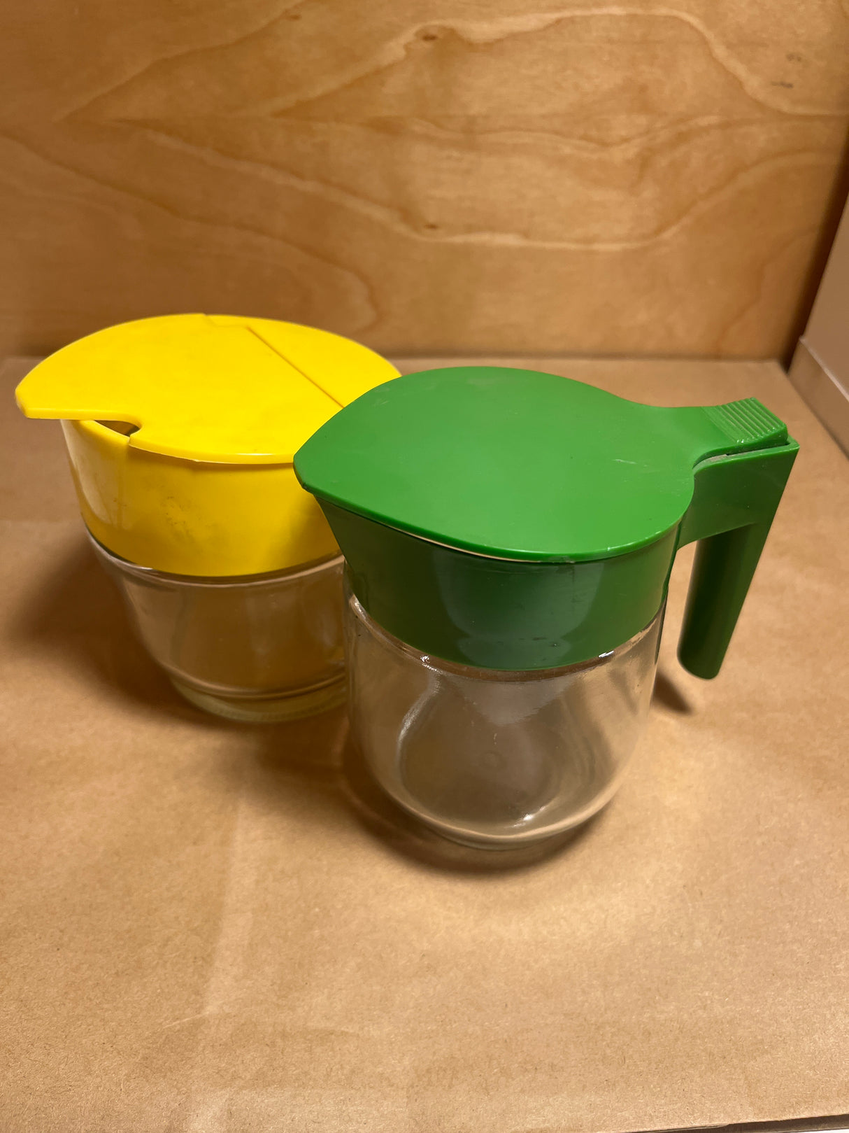 Gemco sugar and cream dispenser set, featuring two clear glass jars with flip-on lids, one with a handle, ideal for syrup or creamer.