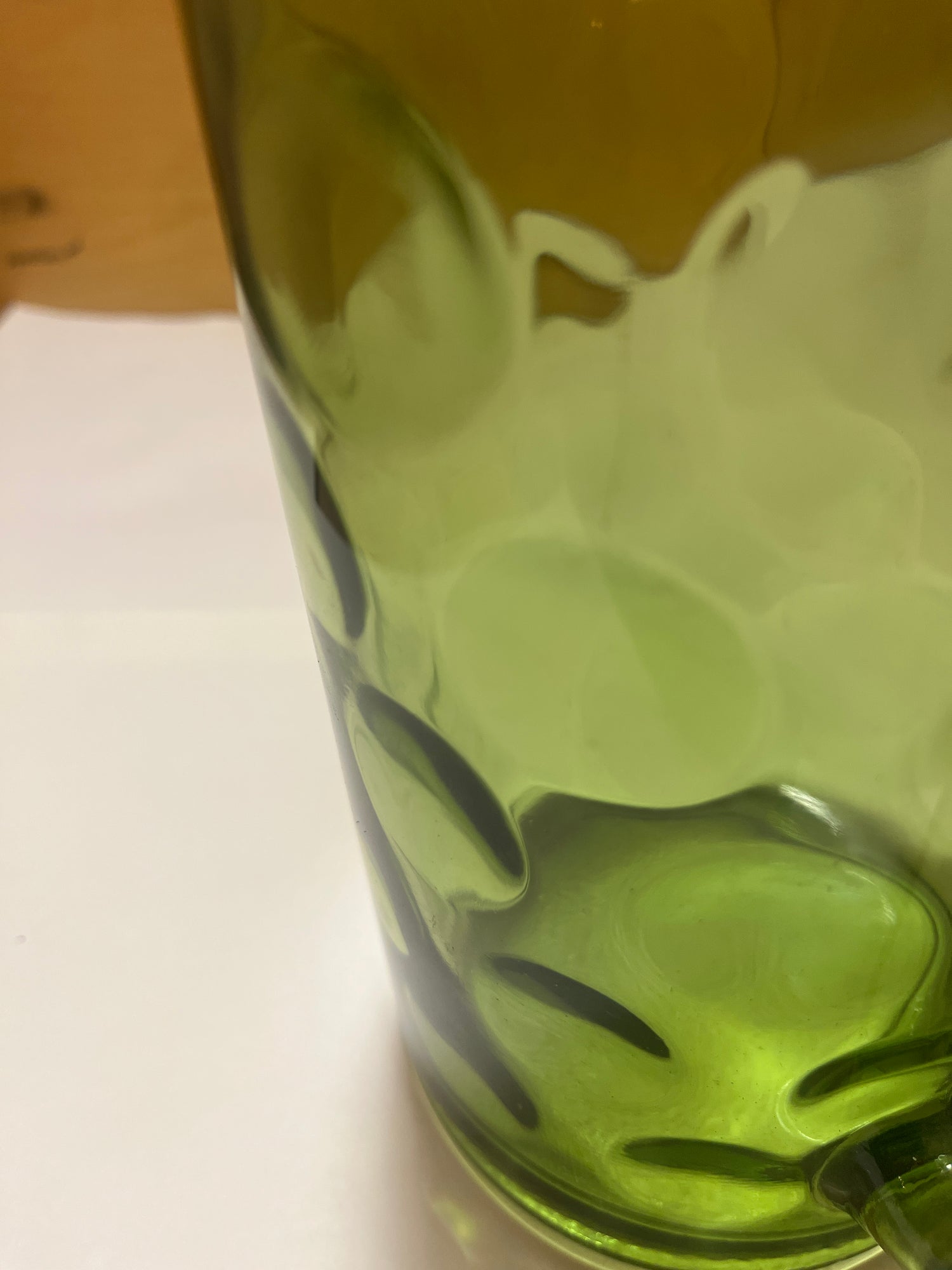 Hazel Atlas Eldorado avocado green coin dot glass pitcher with dimpled texture, shown close-up on a white surface against a wooden background.