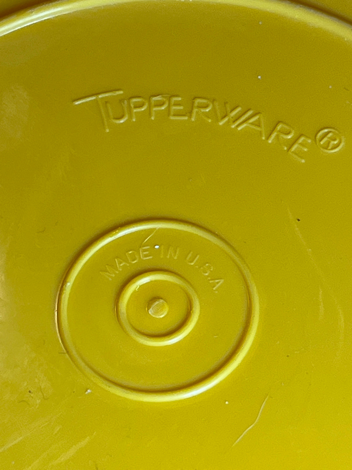 Underside of Tupperware golden yellow pitcher's lid displaying embossed “TUPPERWARE®” logo and “MADE IN U.S.A.” stamp.
