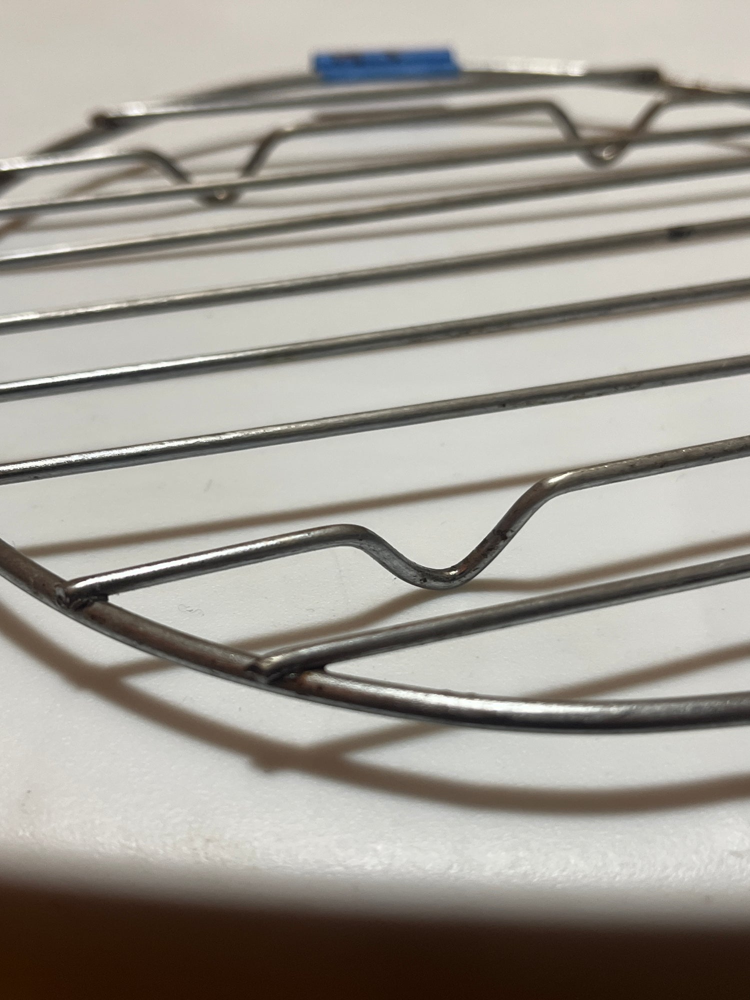Small circular wire cooling rack with raised feet, designed for holding pots and pans. Suitable as a tray or cooling surface for kitchen use.