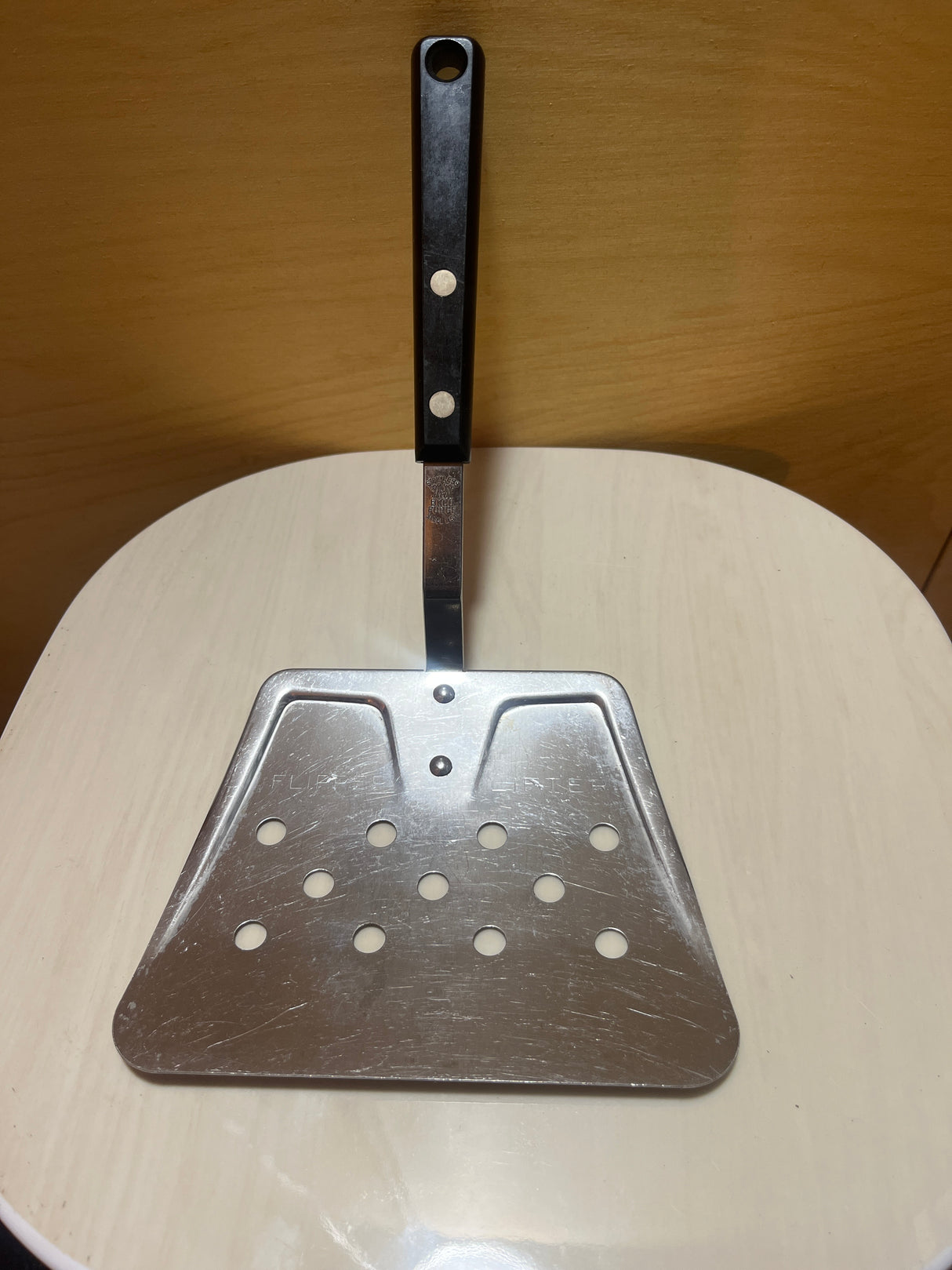 EKCO Flipper Lifter stainless steel spatula, triangular and perforated, with a sturdy black riveted handle, ideal for draining oil while flipping foods on a griddle.