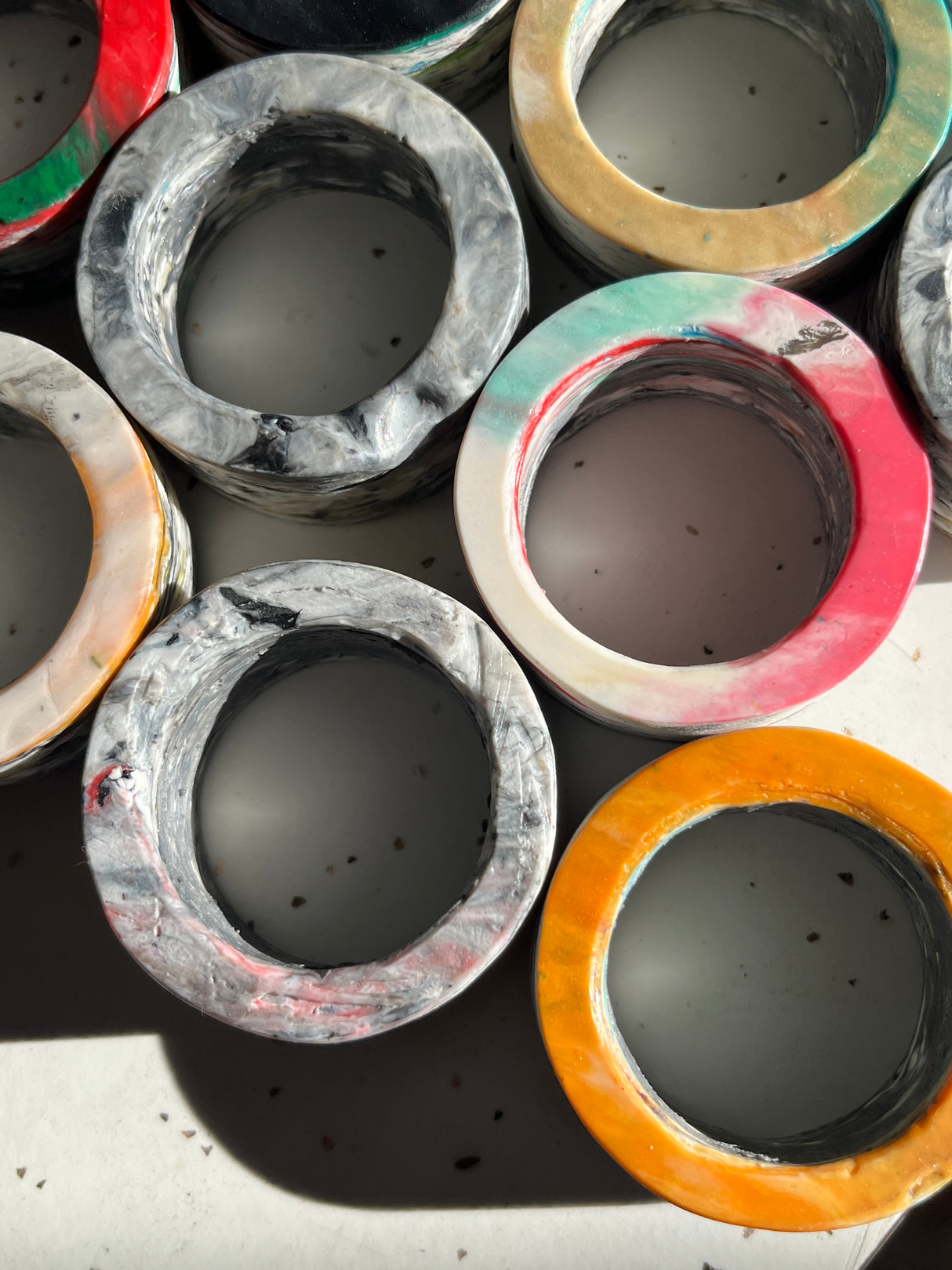 Napkin rings from Reimagined Recycling, featuring unique marbled designs in varied colors, are displayed upside down, highlighting their hollow centers and slightly ridged textures.