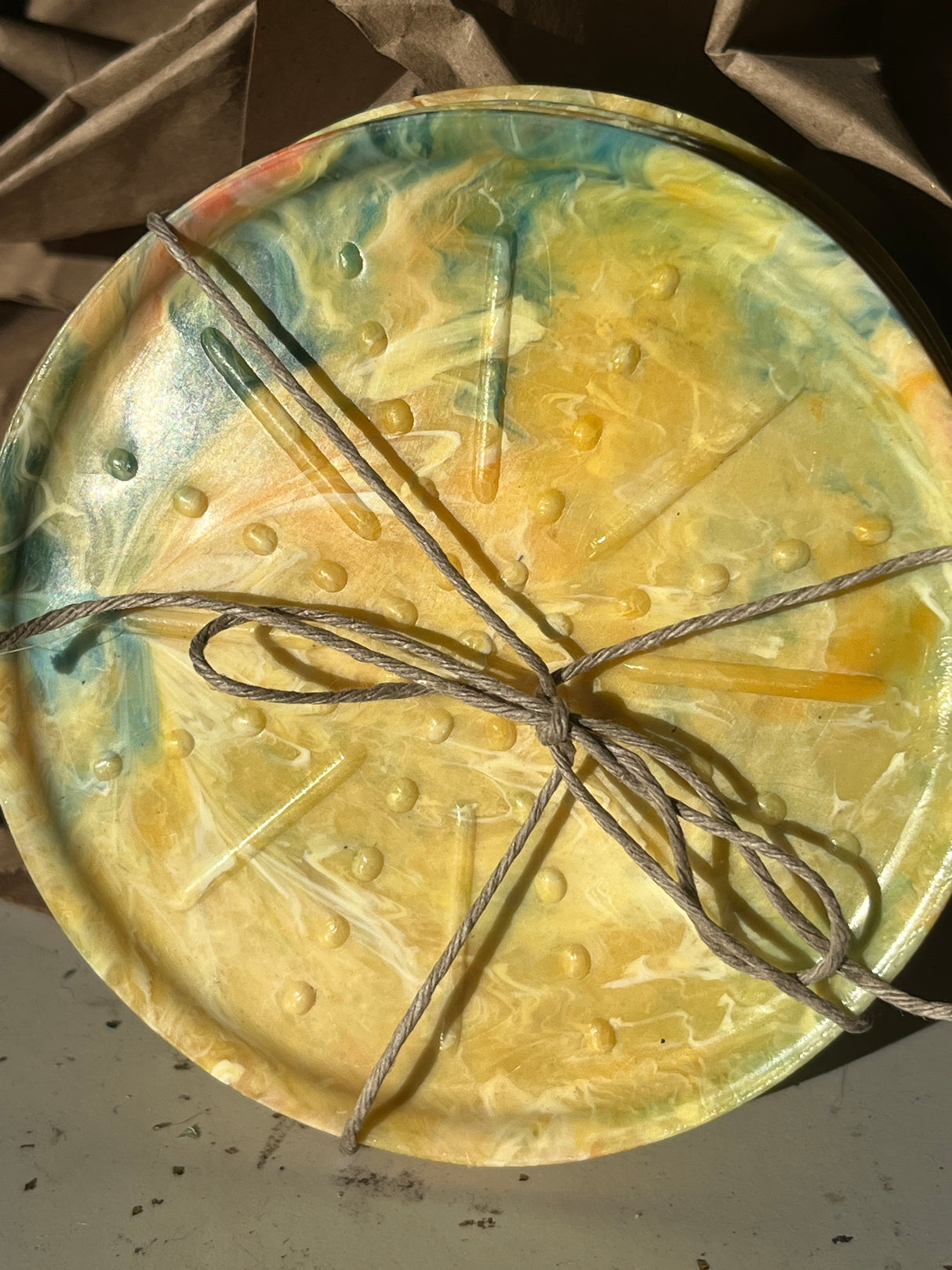 Coaster Sets from Reimagined Recycling: A round, marbled platter with embossed texture, tied with twine on crumpled packing paper, showcasing handmade recycled craftsmanship.