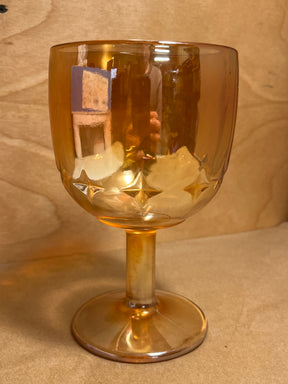 Bartlett Collins Star Marigold Carnival orange glass water goblet with a short stem and rounded bowl, featuring embossed star or diamond motifs, on a wooden surface.
