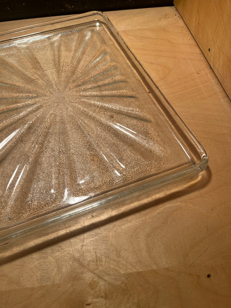 Rectangular glass serving tray featuring a sunburst pattern, placed on a wooden surface, highlighting its textured bottom design.