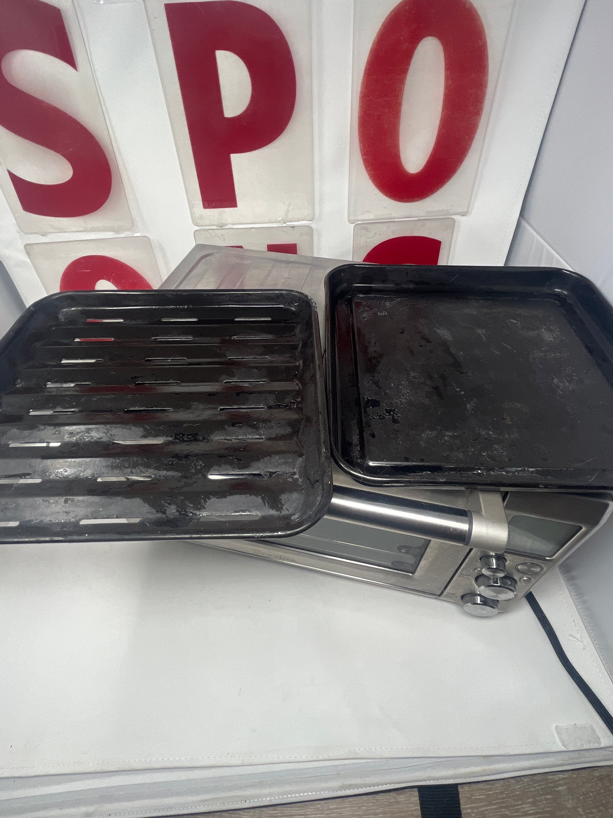 Breville oven with two black rectangular pans and a black grill pan with holes on its surface, showcasing its versatile cooking capabilities.