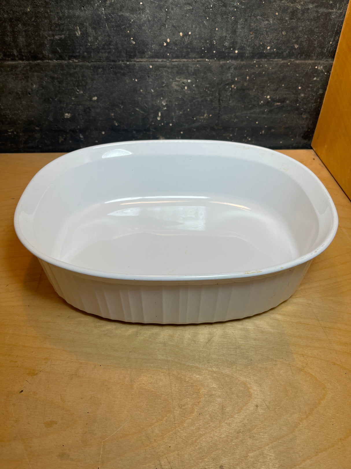 Oval casserole dish - Corning F-2-B French White: 2.5-quart, stoneware with fluted sides and flared rim, ideal for oven use on a wooden surface.