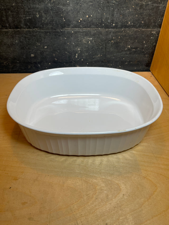 Oval casserole dish - Corning F-2-B French White: 2.5-quart, stoneware with fluted sides and flared rim, ideal for oven use on a wooden surface.