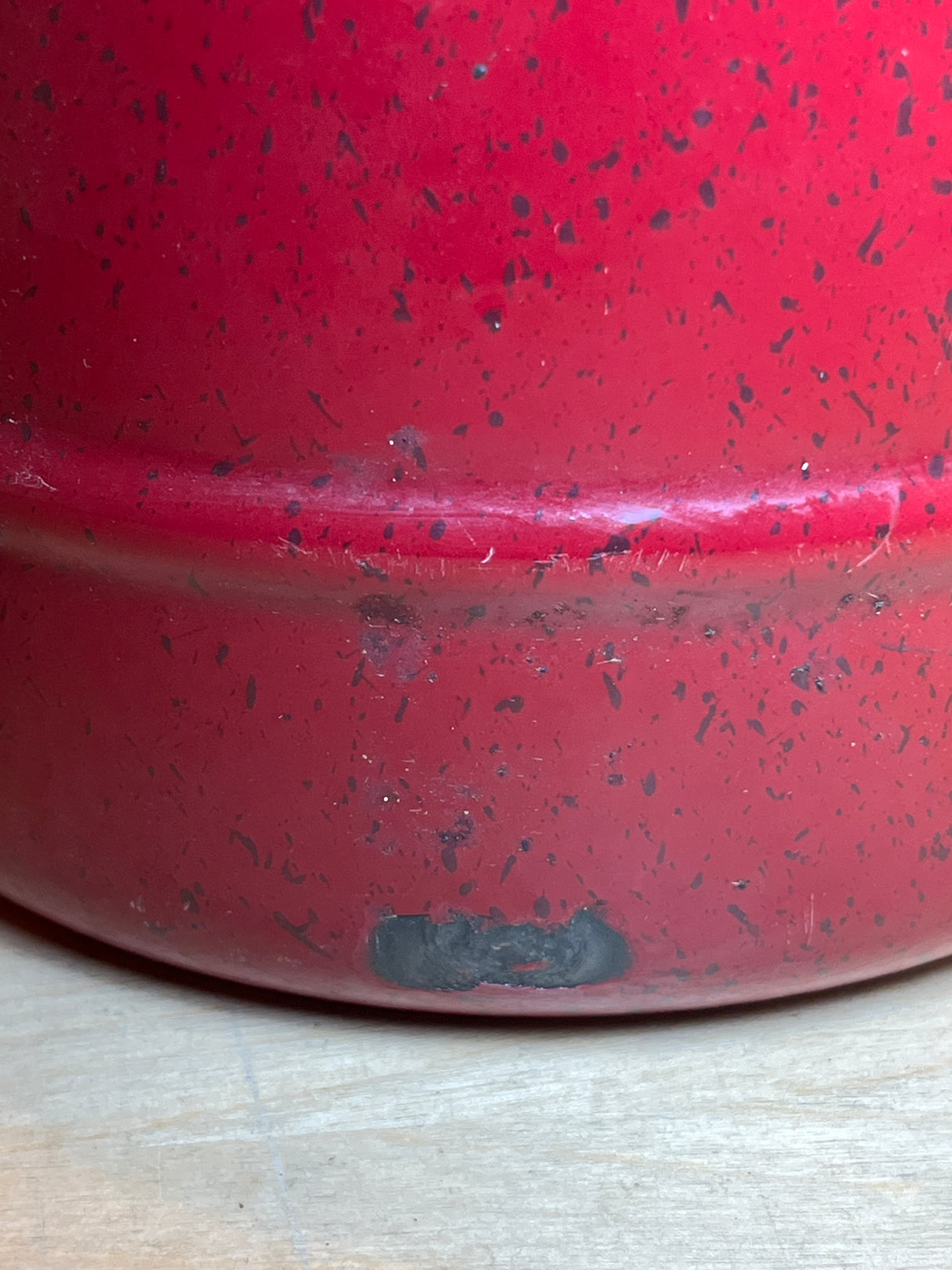 Tea kettle - steel red speckled enamelware - Paula Deen, showing a chipped area near the bottom revealing darker metal, sitting on a wooden surface.