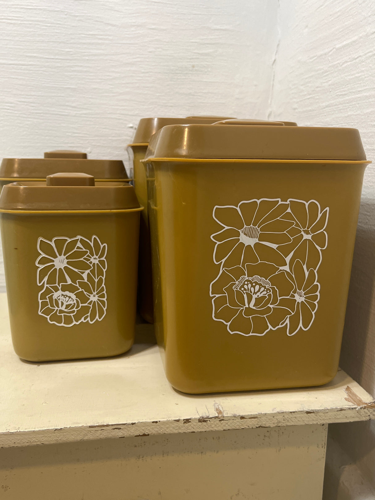 Melmac set of 4 retro food storage containers in mustard with white floral illustrations, featuring snap-on lids; second-largest container shows a small crack.