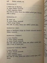 Trader Vic’s Bartender’s Guide (Revised 1972) open to a page detailing five Manhattan cocktail variations, showcasing ingredients and preparation methods. Book shows slight corner wear.