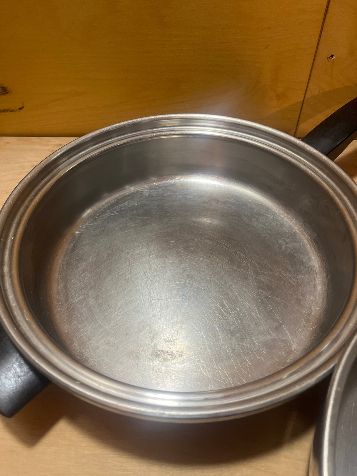 Seal-O-Matic Thermium Multi-Plex 18-8 Stainless Steel 11” Skillet with Lid, featuring a black handle, sits empty on a wooden surface.