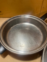 Seal-O-Matic Thermium Multi-Plex 18-8 Stainless Steel 11” Skillet with Lid, featuring a black handle, sits empty on a wooden surface.