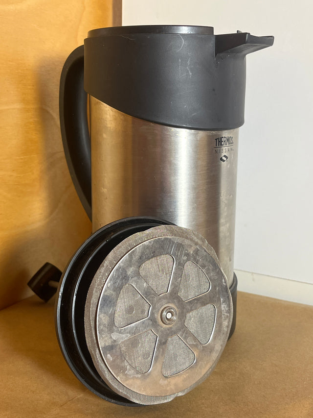 Thermos Nissan stainless steel insulated French press coffee maker with visible French-press plunger/filter assembly resting beside it, highlighting its vacuum-insulated design.
