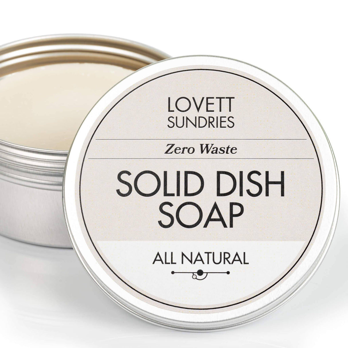 Small metal tin with Lovett Sundries label, containing solid dish soap puck. Zero waste, all-natural formula, lid slightly ajar, emphasizing eco-friendly cleaning.
