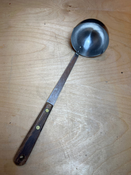 Vintage Robinson stainless steel ladle with a long wooden handle, featuring a hanging hole and two indents to prevent splattering, on a wooden surface.