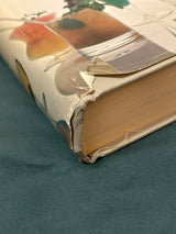 Trader Vic's Bartender's Guide (Revised 1972) showing a worn dust jacket corner, revealing cloth binding and page block, on a teal fabric surface.