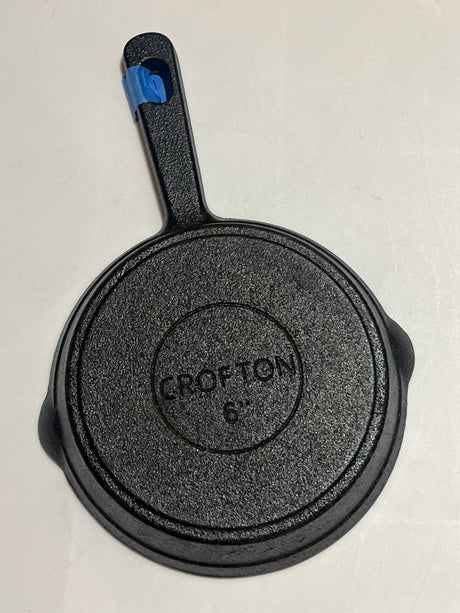 Crofton 6” teeny cast iron frying pan, underside view with Crofton 6″ label, handle wrapped in blue painter's tape, ideal for baking or frying.