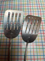Flat thin steel slotted spatula with wood handle, featuring a broad, flat head with long slots, ideal for flipping and transferring hot foods.