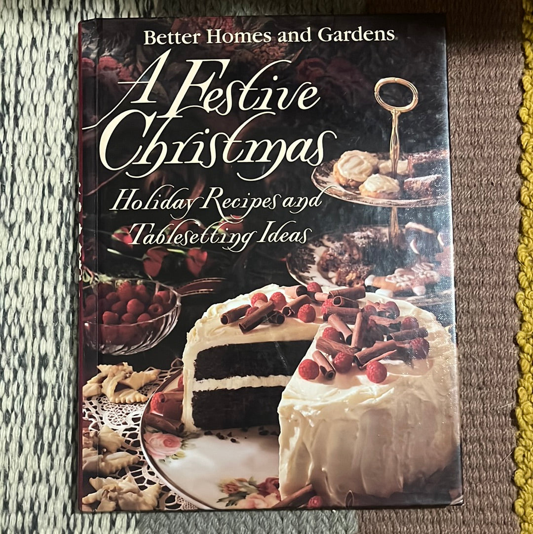 A Festive Christmas: Holiday Recipes and Tablesetting Ideas book on a table, featuring a Buttermilk Chocolate Cake with white frosting and berries on the cover.