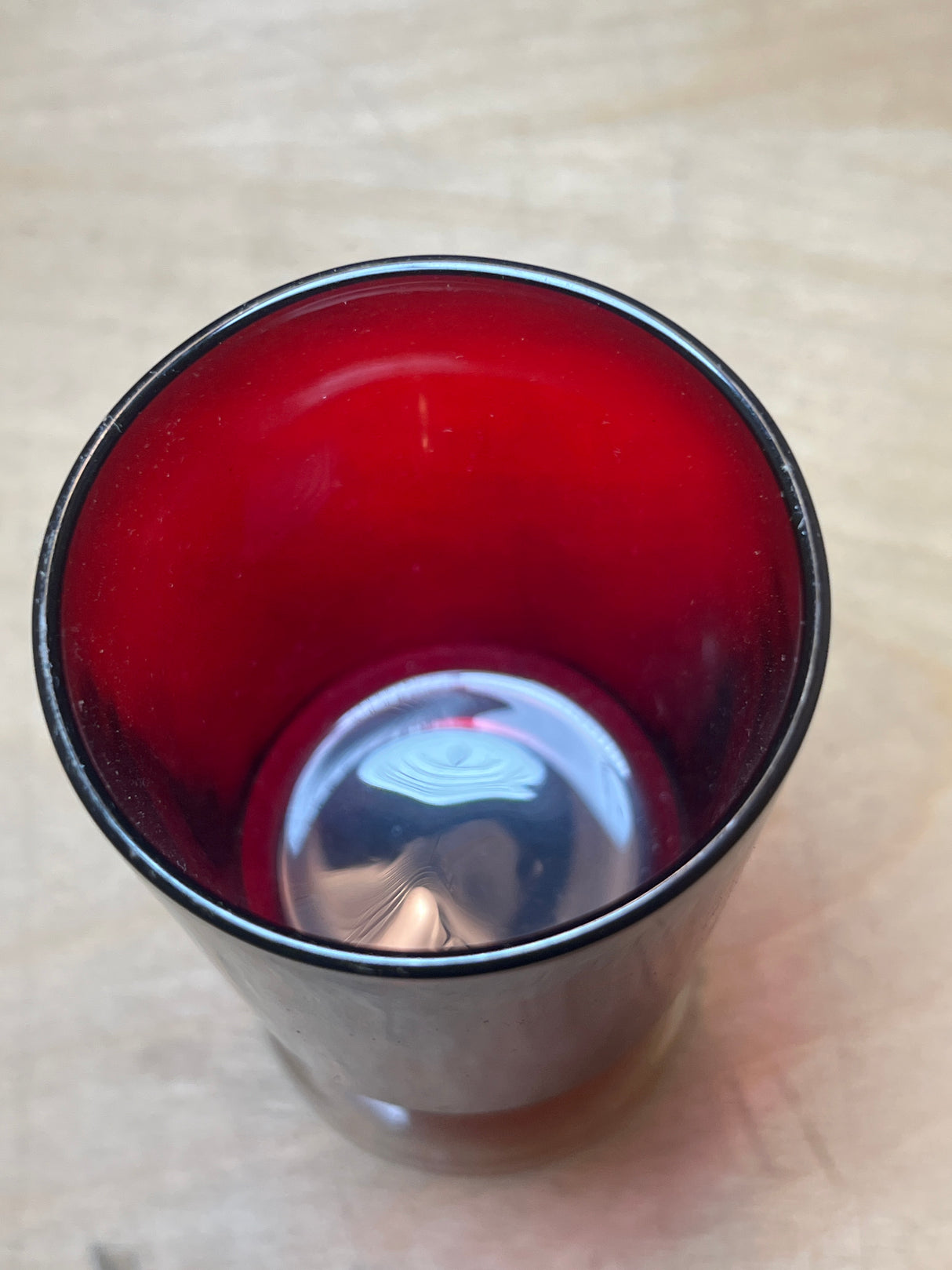 Luminarc/ARCOROC ruby red small wine glass, double-walled stainless-steel exterior, deep red interior, empty, reflecting light on a light wood surface.