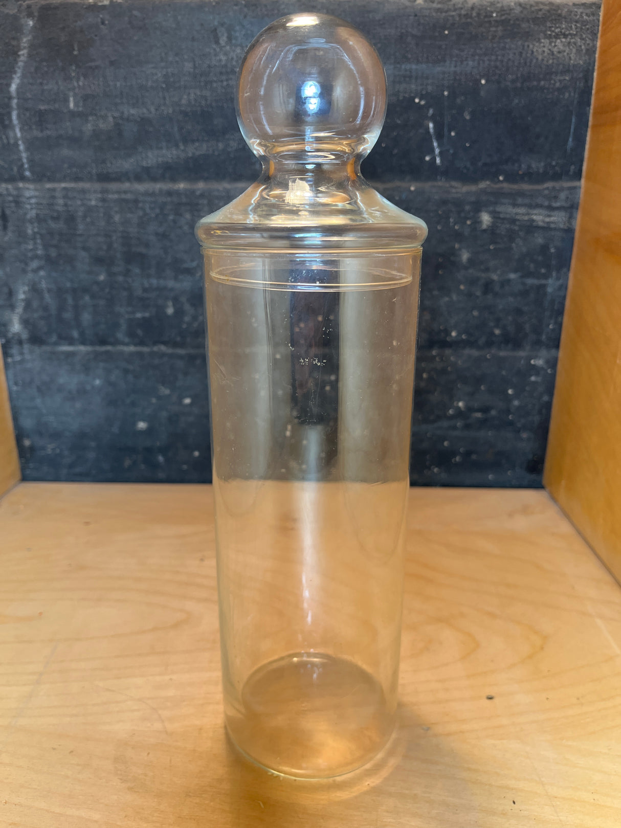 Libbey tall apothecary jar with a lid, featuring a cylindrical design and round knob, displayed on a wooden surface.