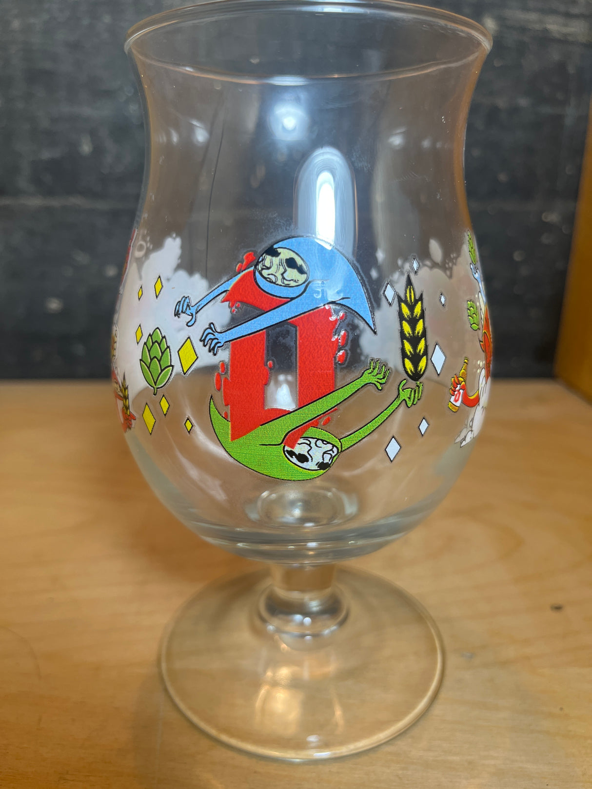 Huvel Belgian beer glass featuring the 2024 limited edition JT Samuels illustration with sloth-like creatures and stylized hops on a tulip-shaped bowl.