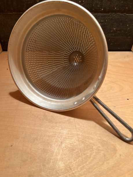 Cone sieve strainer with wide base - aluminum unknown brand; vintage design, sturdy construction, long wire handle, ideal for food preservation, resting on wooden surface.