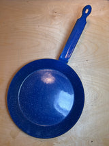 Blue speckled enamelware fry pan with long handle on wood surface, ideal for camping. Minor enamel damage on rim, perfect for outdoor cooking.