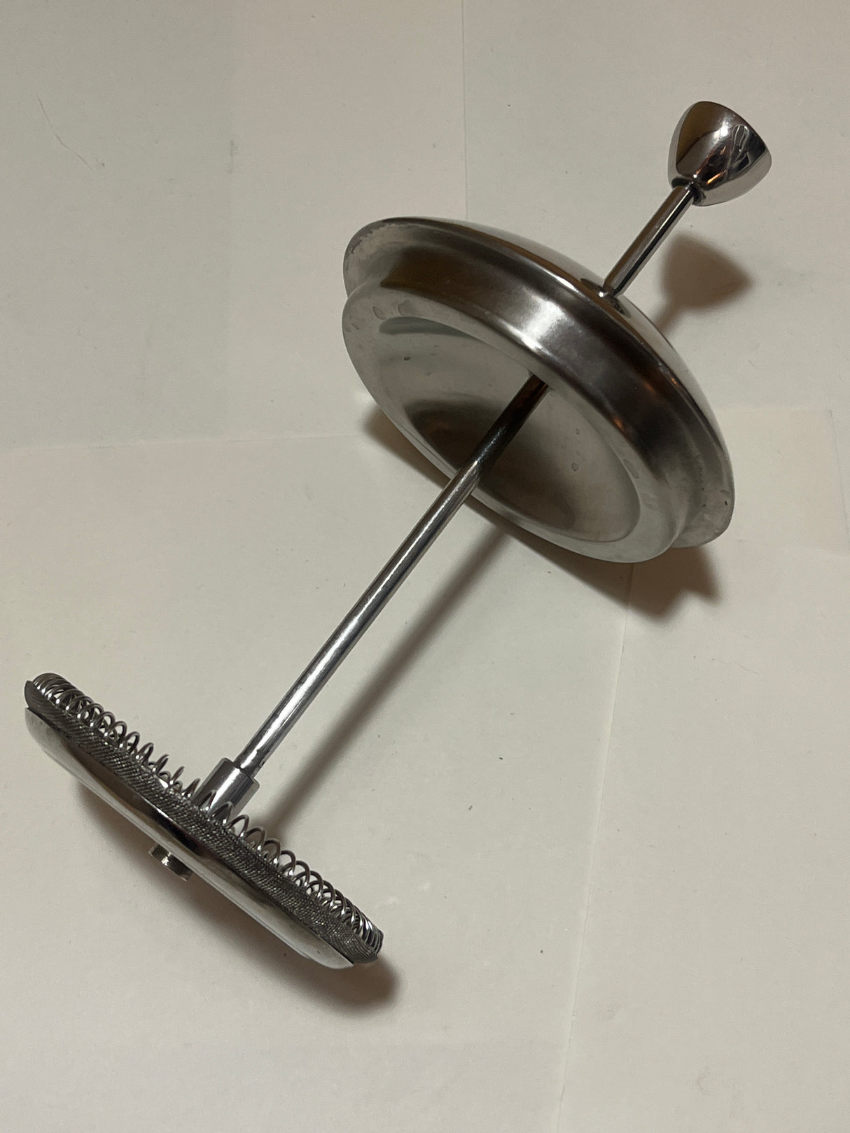 Frieling stainless steel French press coffee maker's plunger/filter assembly featuring a central rod, metal disc, and fine-mesh screen with a coiled spring edge.
