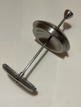 Frieling stainless steel French press coffee maker's plunger/filter assembly featuring a central rod, metal disc, and fine-mesh screen with a coiled spring edge.