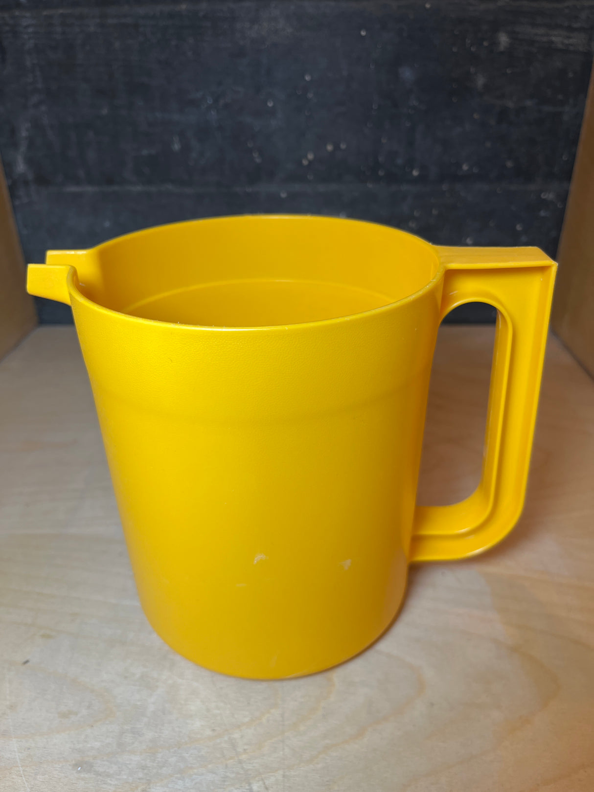Tupperware golden yellow pitcher with straight sides, a built-in handle, and a small pouring spout, displayed empty on a wooden surface.
